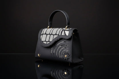 ELVI CREATION Elsha black vegan leather handbag with black and white wax flap and spiral cutouts.