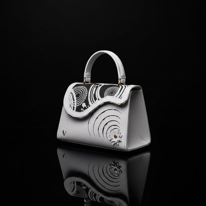 ELVI CREATION Elsha white vegan leather handbag with black and white wax print flap and spiral cut-outs.