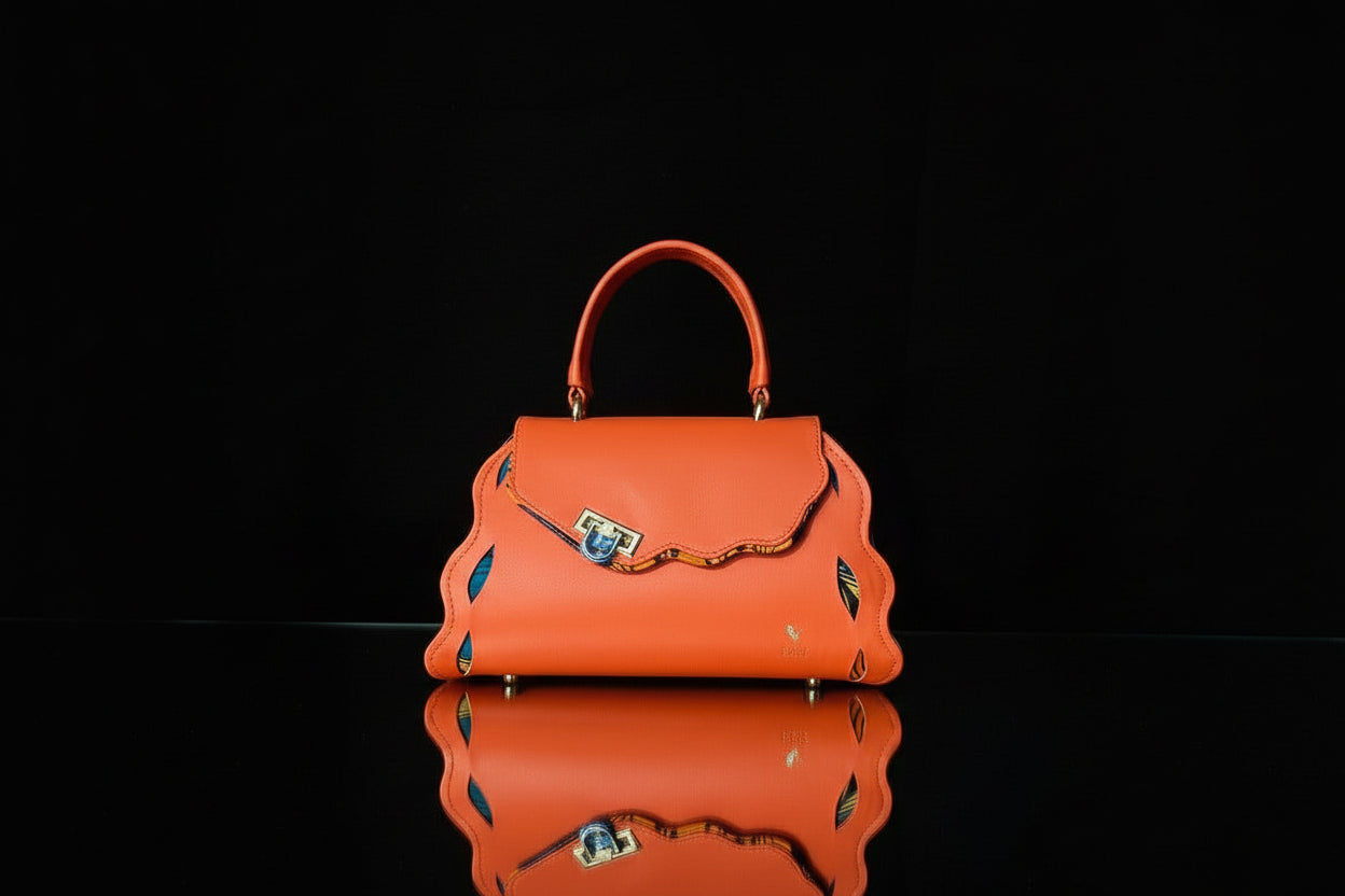 ELVI CREATION Trésor orange vegan leather handbag with wavy edges and patterned lining. Features gold hardware and a clasp closure.