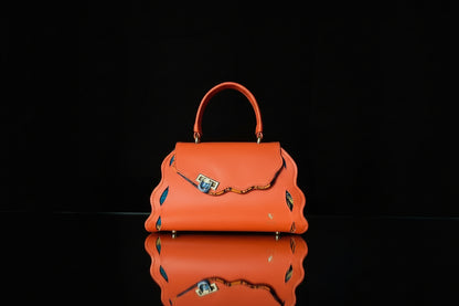 ELVI CREATION Trésor orange vegan leather handbag with wavy edges and patterned lining. Features gold hardware and a clasp closure.